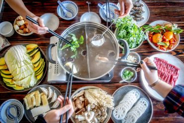 A birds-eye vide of a large festival table with a hotpot in the middle, slices of meat and plates of vegetables surrounding it.