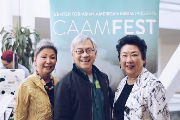 Three people at the CAAMFest 2018 Preview Screening standing in front of a CAAMFest banner and smiling.