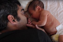 A South Asian man is on the bed facing his newborn son.