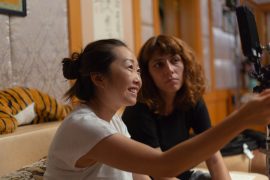 An Asian American film director, Lulu Wang, has her hair in a ponytail bun and smiles while she's pointing. She is the director of "The Farewell."