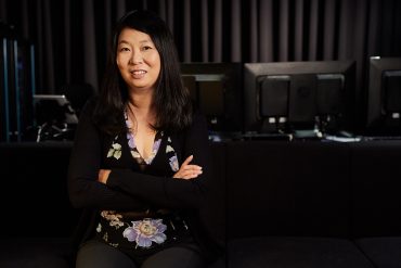 A Chinese American woman with straight hair crosses her arms and smiles for the camera.