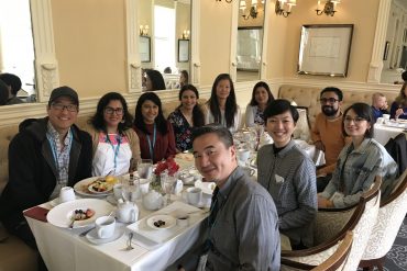 A group of mixed Asian Americans sit at a well lit dining table and smile at the camera.