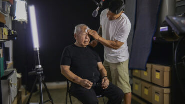 Man in white shirt putting make up on man sitting down
